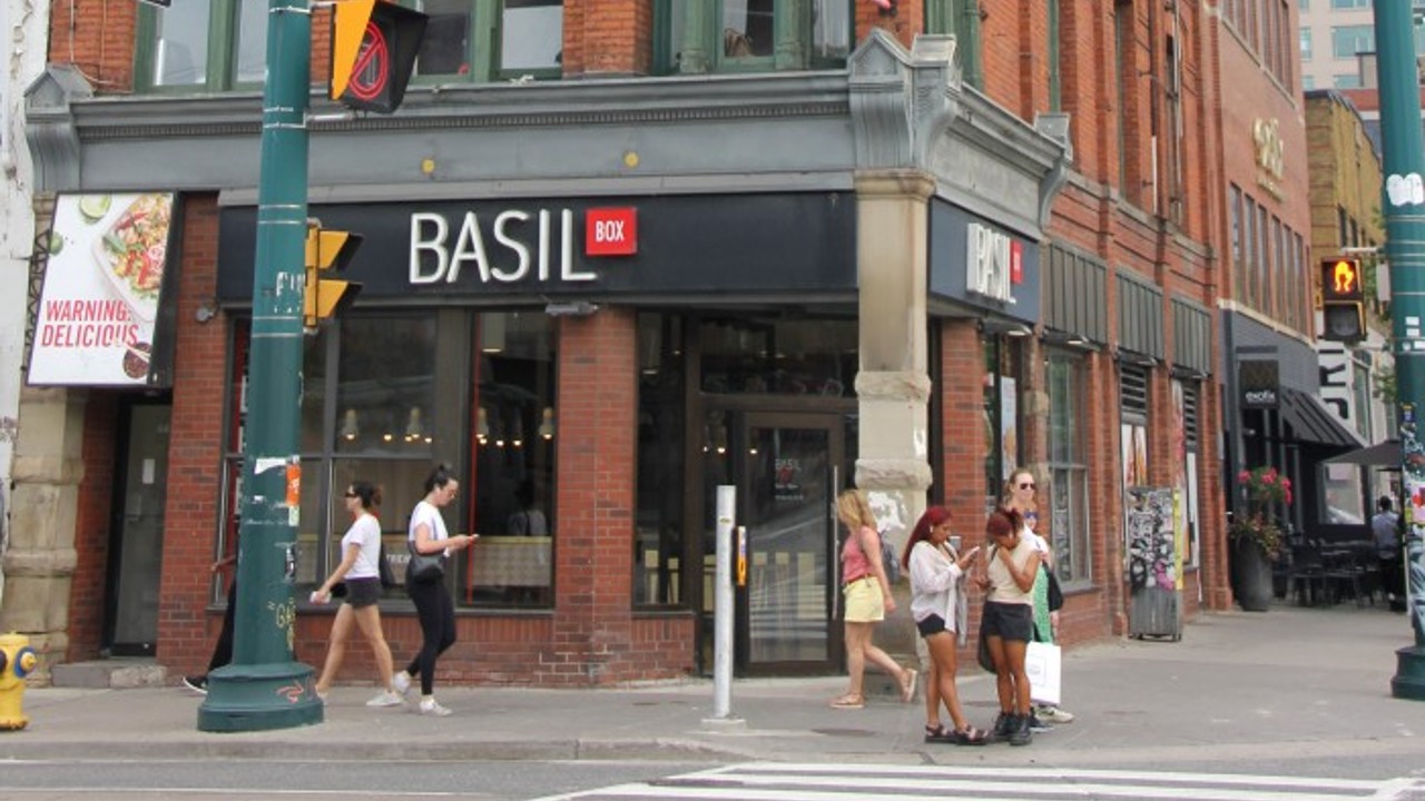 A three-story brick building on Queen St. W. in Toronto with a restaurant called Basil Box on the ground level