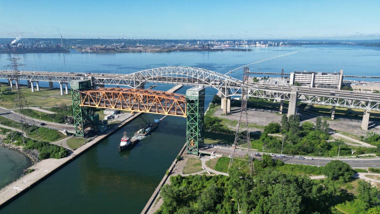 A tug boat pulls a long floating intake pipe out of Hamilton’s harbour