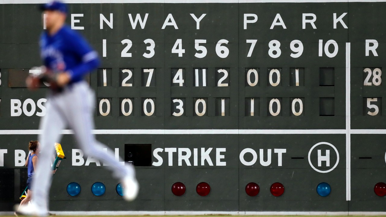 A Toronto Blue Jays player runs in front of the Fenway Park scoreboard