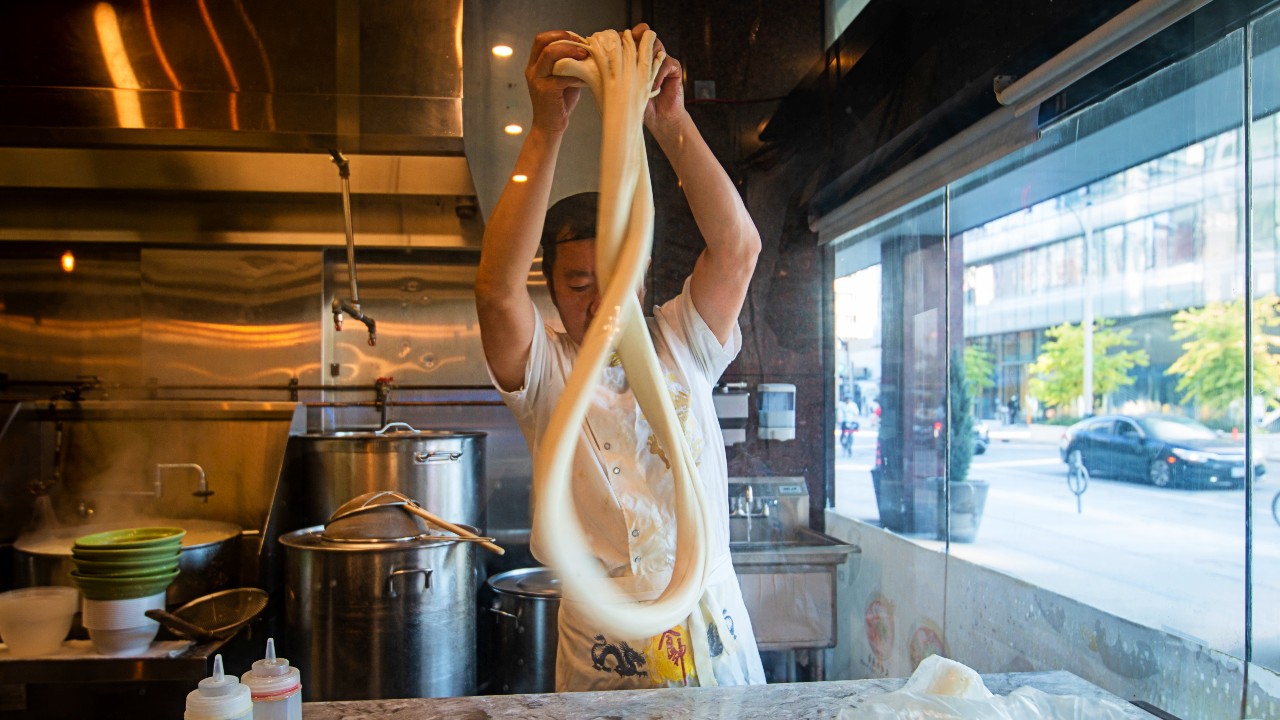 A chef at Yee’s Hand Pulled Noodles in Toronto works with lā miàn dough in the window of the restaraunt